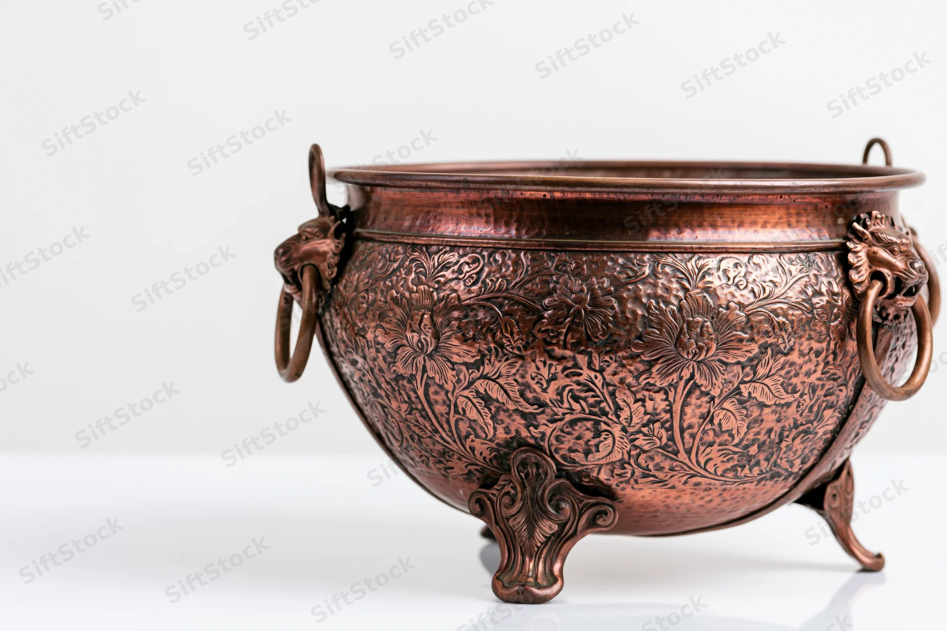 Antique hammered copper planter with floral embossing and lion head handles on white surface