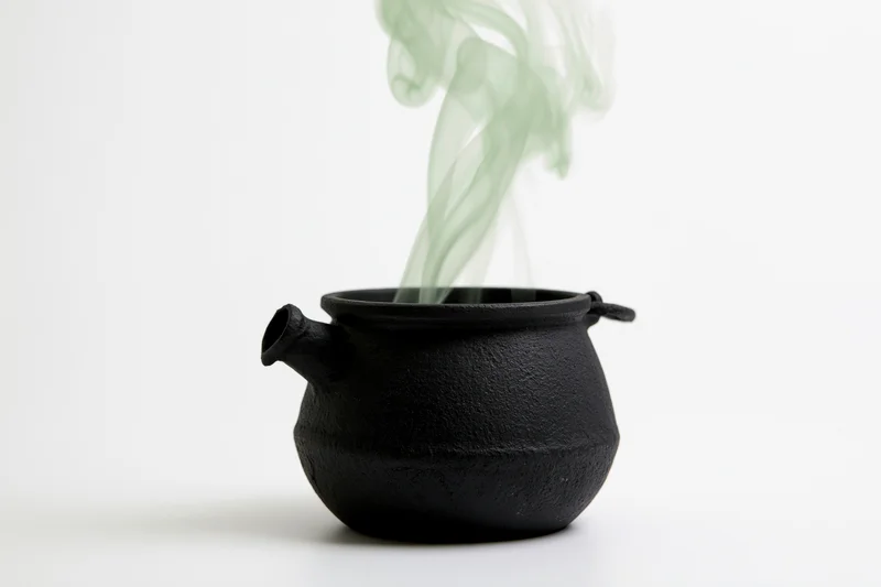 Black cast iron cauldron emitting green smoke on white background