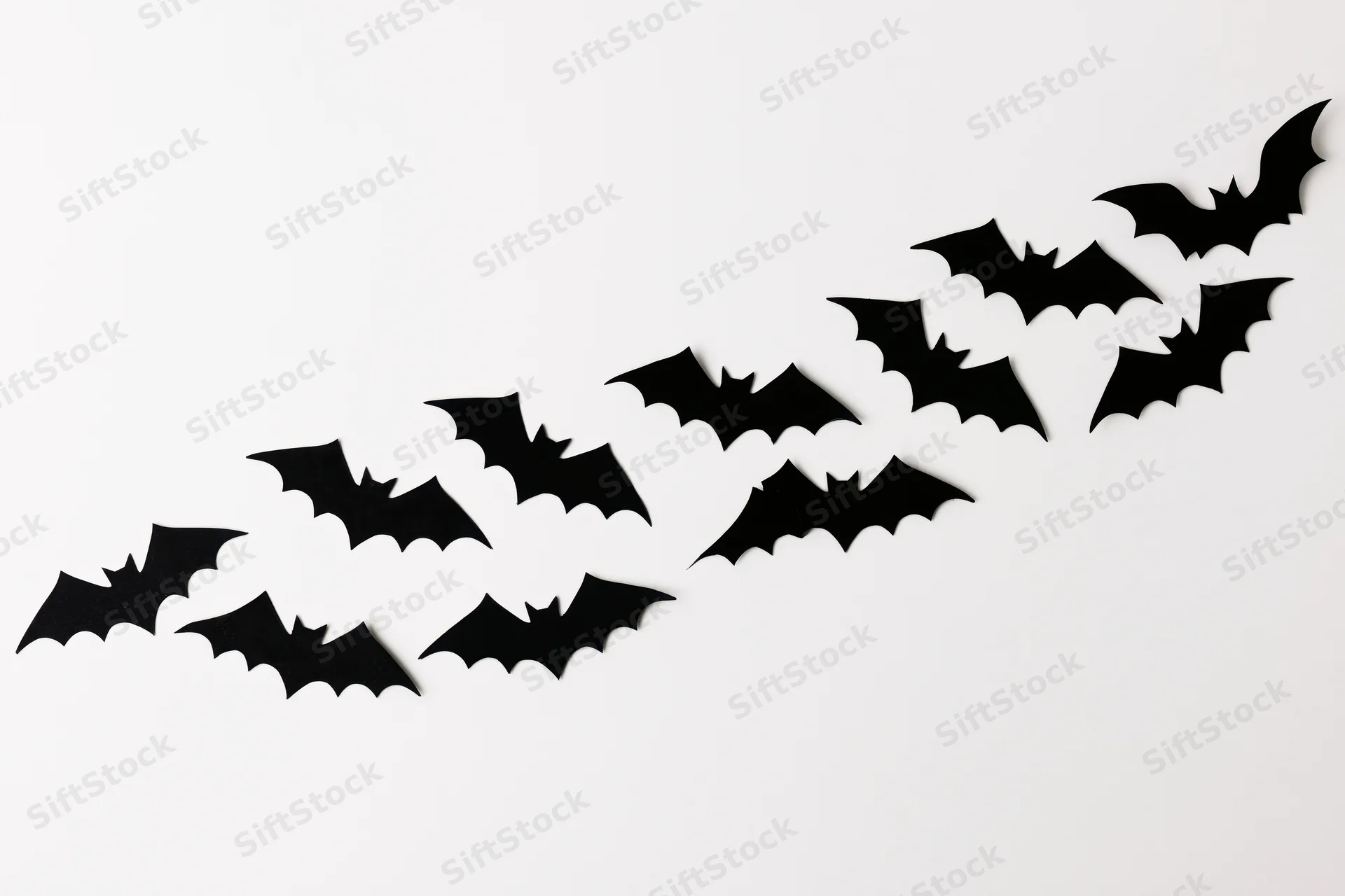 Black paper bat cutouts arranged in diagonal swarm pattern on white surface