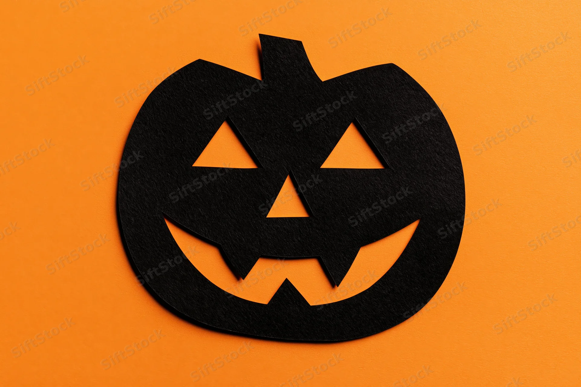 Black paper jack-o-lantern cutout on orange background