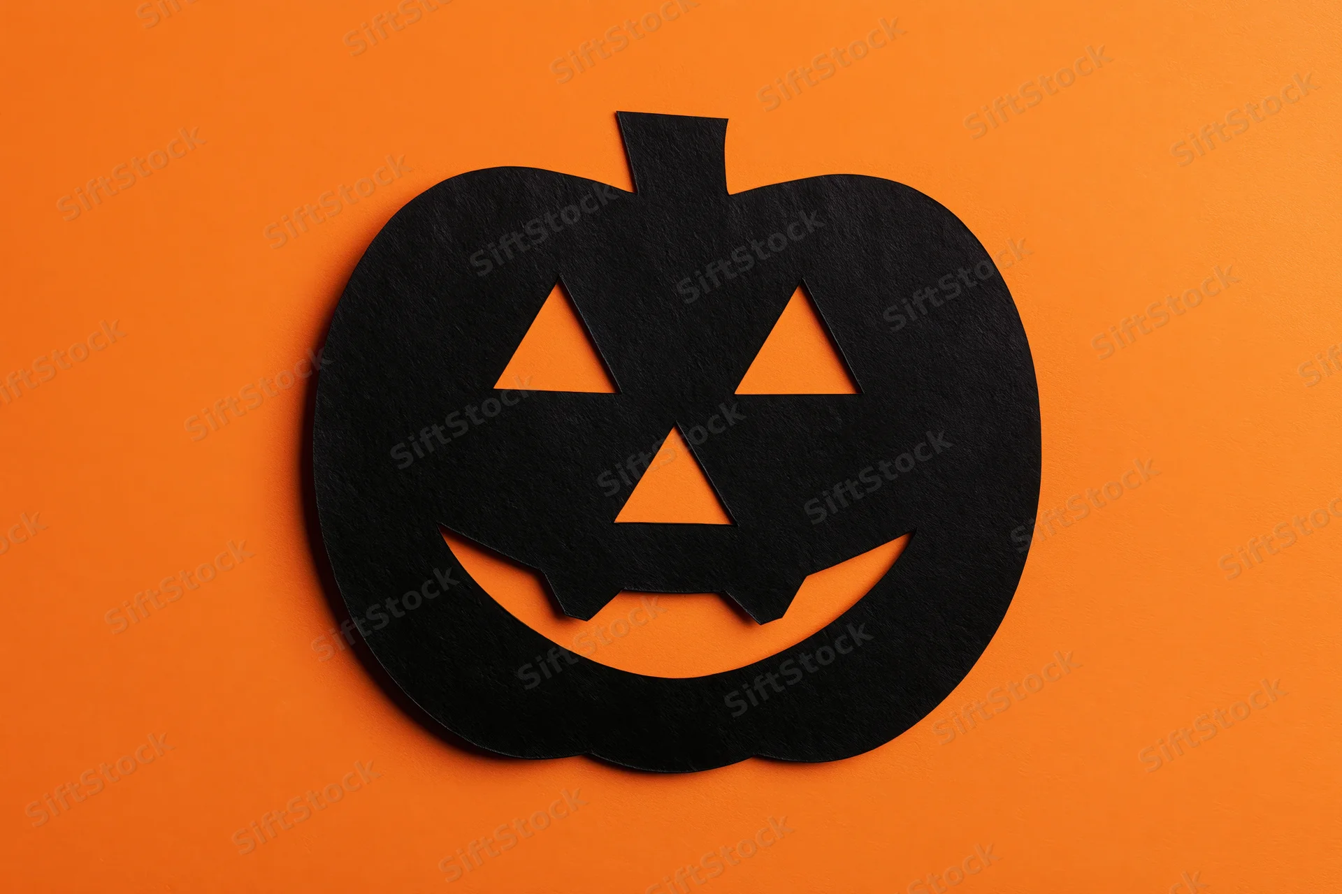 Black paper jack-o-lantern cutout on orange background