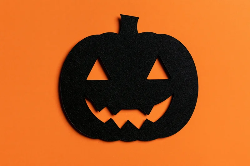 Black paper cut-out jack-o-lantern silhouette on orange background