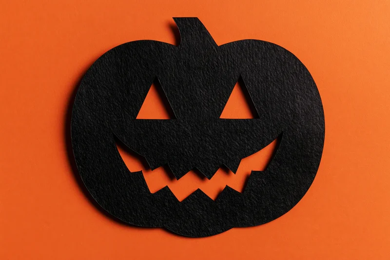 Black paper jack-o-lantern cutout on orange background with copyspace