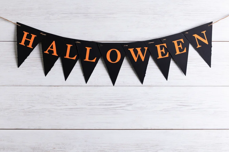 Black paper pennant banner spelling halloween in orange letters hanging on white wooden wall