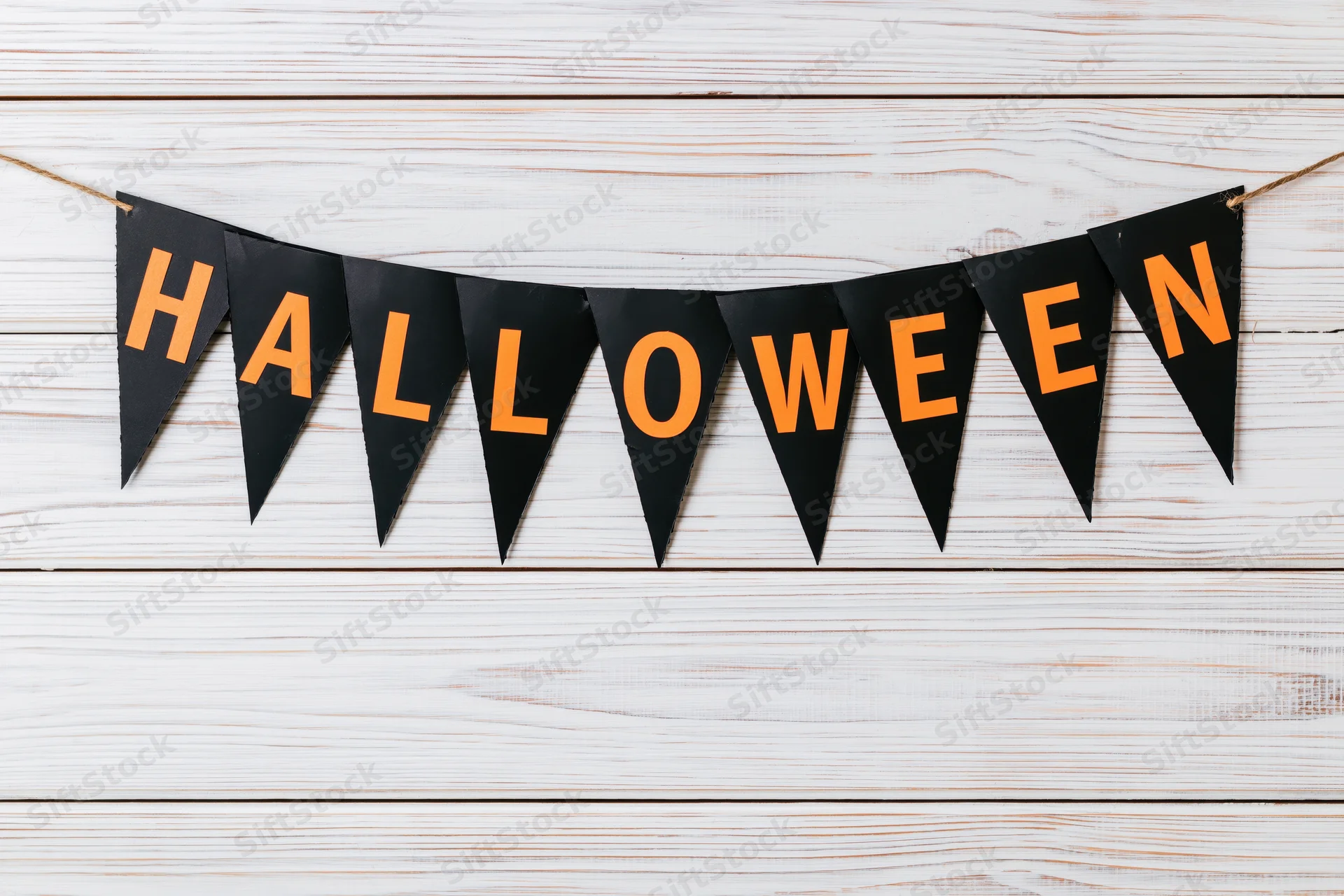 Black paper pennant banner spelling halloween in orange letters hanging on white wooden wall
