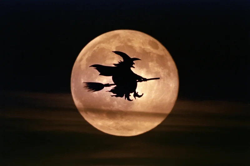 Witch flying on broomstick silhouetted against full moon in night sky