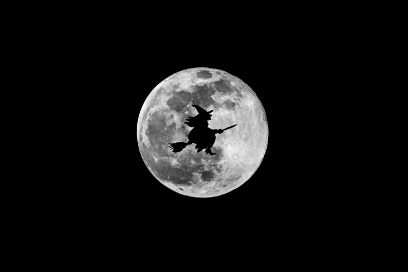 Witch flying on broomstick silhouetted against full moon in dark night sky