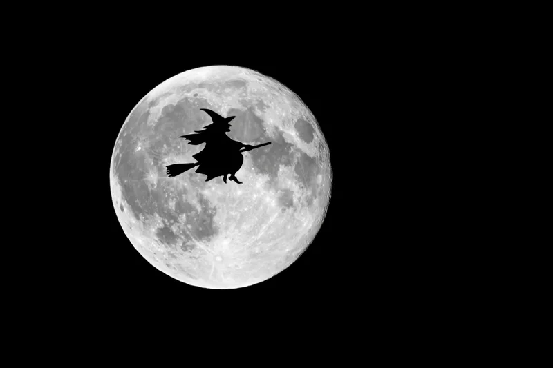 Witch flying on broomstick in front of full moon at night