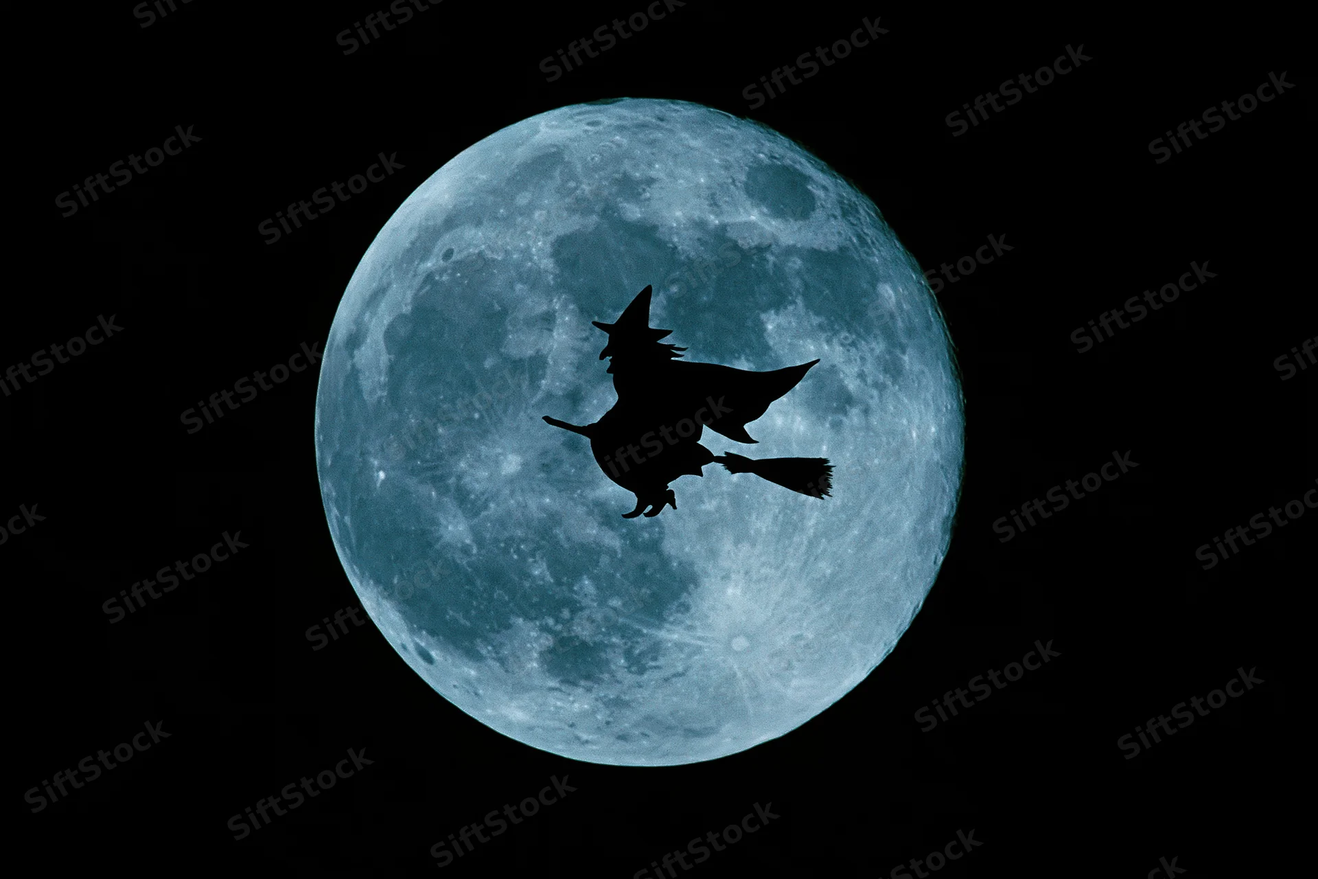 Witch flying on broomstick silhouetted against full blue moon in night sky