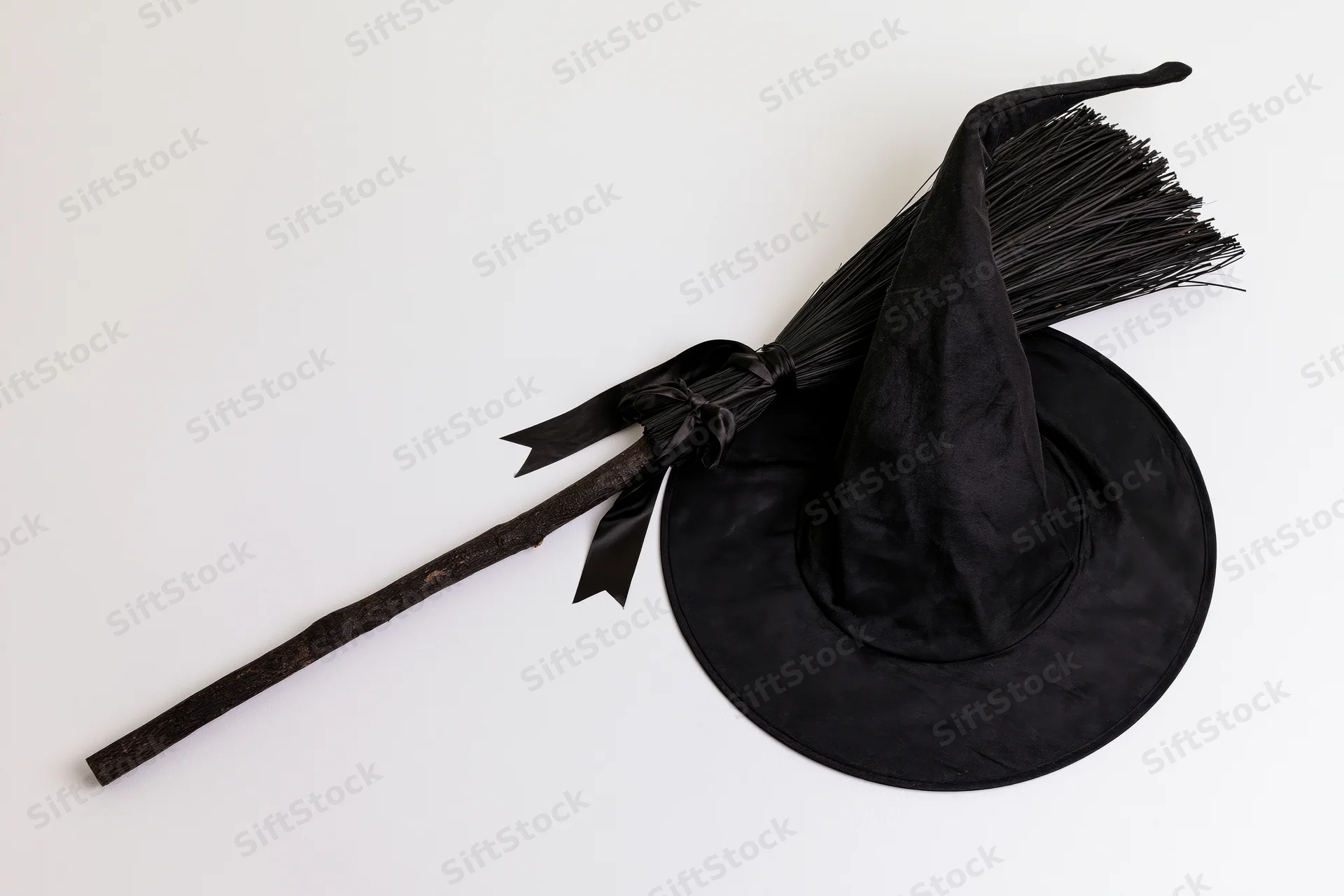 Black witch hat with crooked point and dark broom on white surface