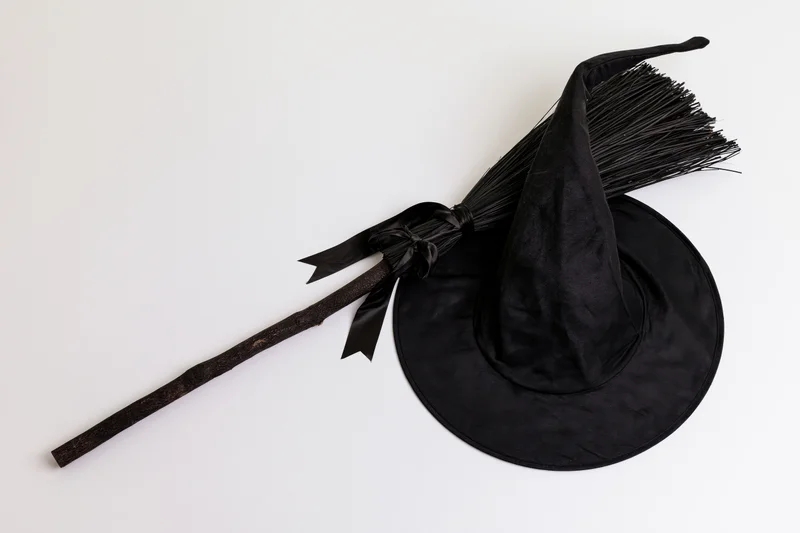 Black witch hat with crooked point and dark broom on white surface