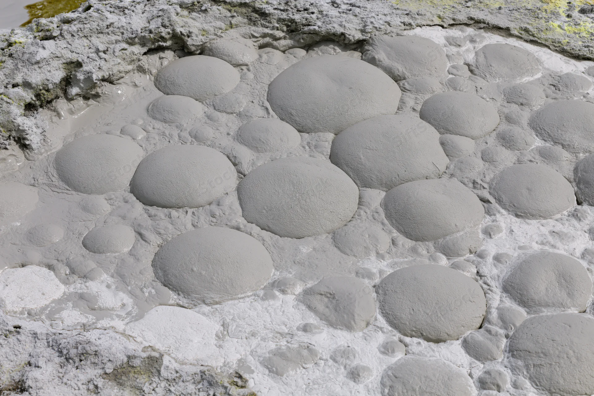 Boiling mud pool with dome-shaped blisters on geothermal landscape