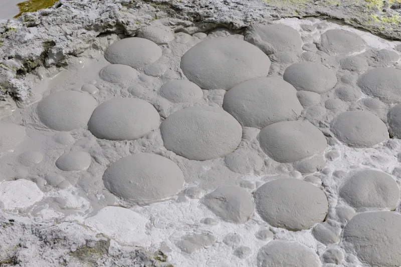 Boiling mud pool with dome-shaped blisters on geothermal landscape