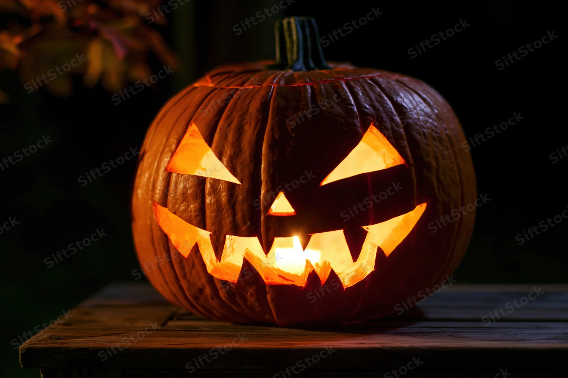 Carved pumpkin glowing with candlelight on wooden table at night