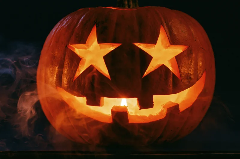 Carved pumpkin with star-shaped eyes and wide grin glowing from within at night