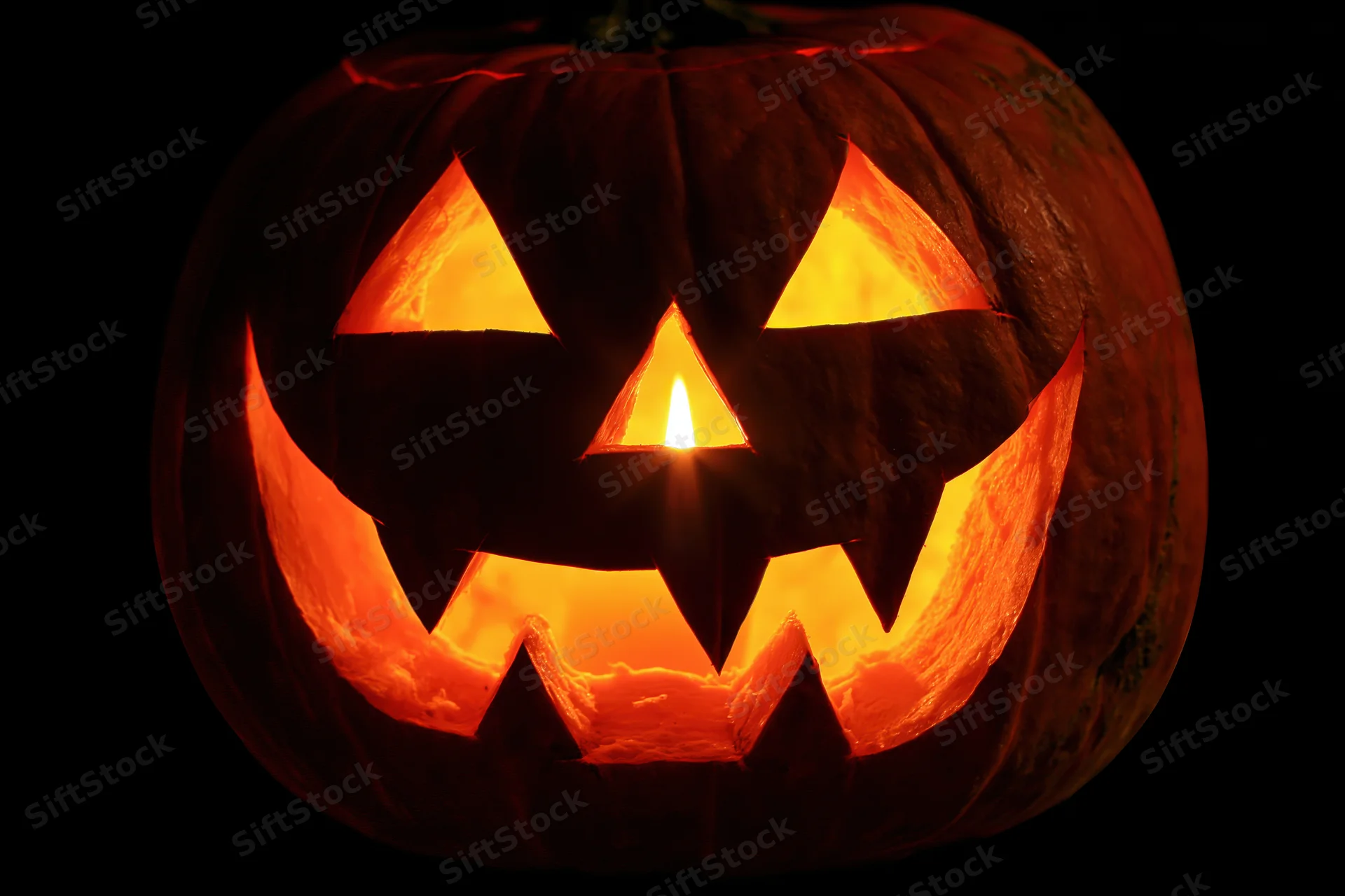 Carved pumpkin with glowing face lit from within against dark background