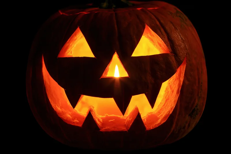 Carved pumpkin with glowing face lit from within against dark background
