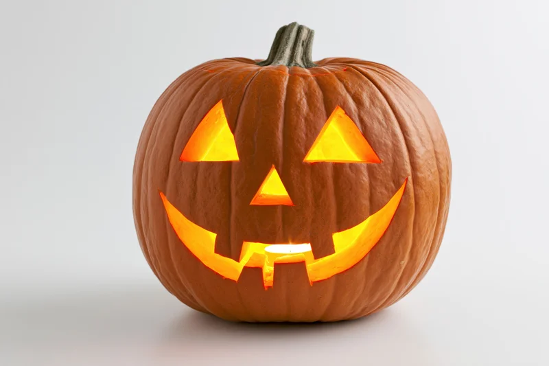 Carved pumpkin with glowing smile face lit by candle on white background