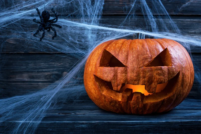 Carved pumpkin with glowing face and spider web on dark wooden surface