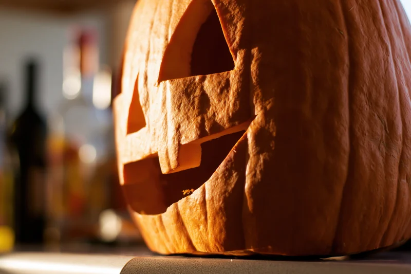 Carved pumpkin with triangular eyes and jagged mouth glowing on kitchen counter