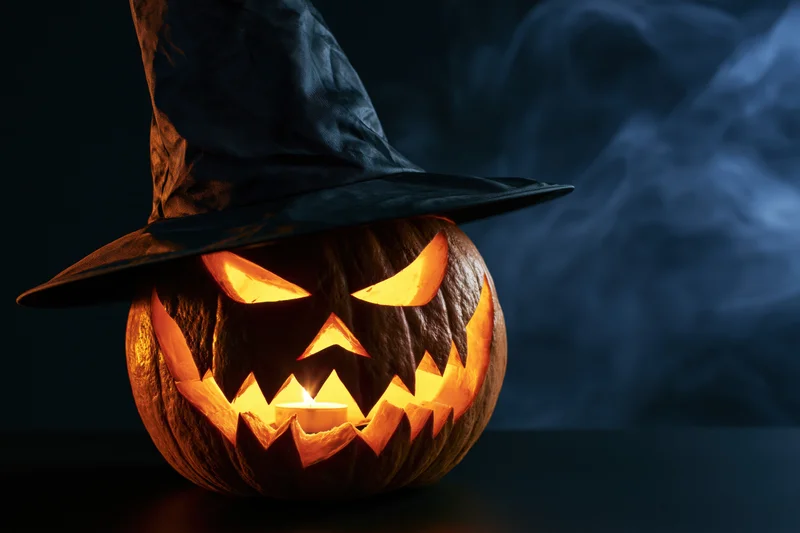Carved jack-o-lantern with glowing face and black witch hat on dark smoky background