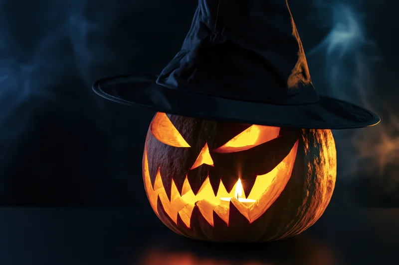 Carved jack-o-lantern with witch hat glowing from candlelight in dark smoky setting
