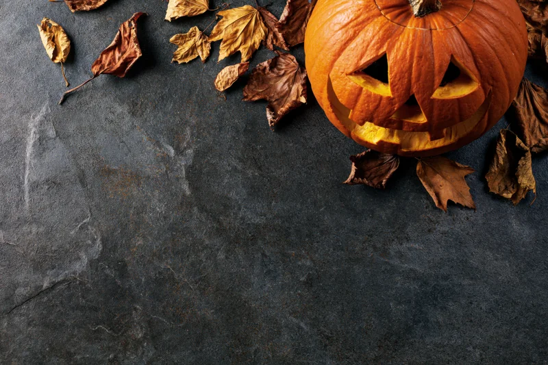 Carved pumpkin with triangular eyes and dried leaves on dark stone surface