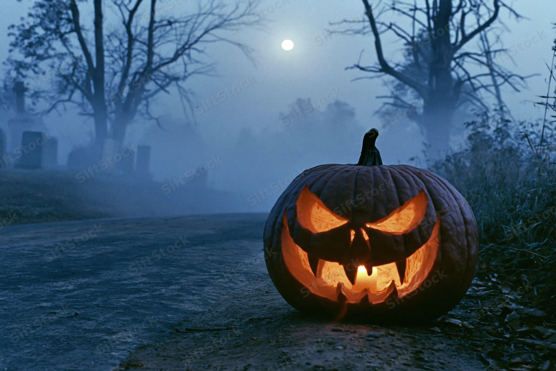Carved jack-o-lantern with glowing menacing face on a foggy graveyard path at night