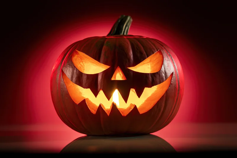 Carved pumpkin with glowing face lit from within on dark red background