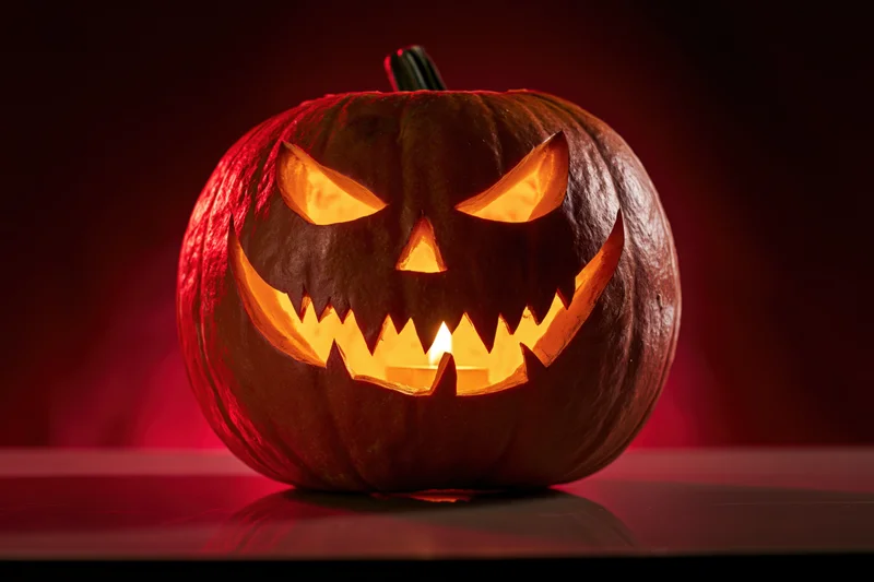 Carved pumpkin with glowing jack-o-lantern face sitting on a dark surface