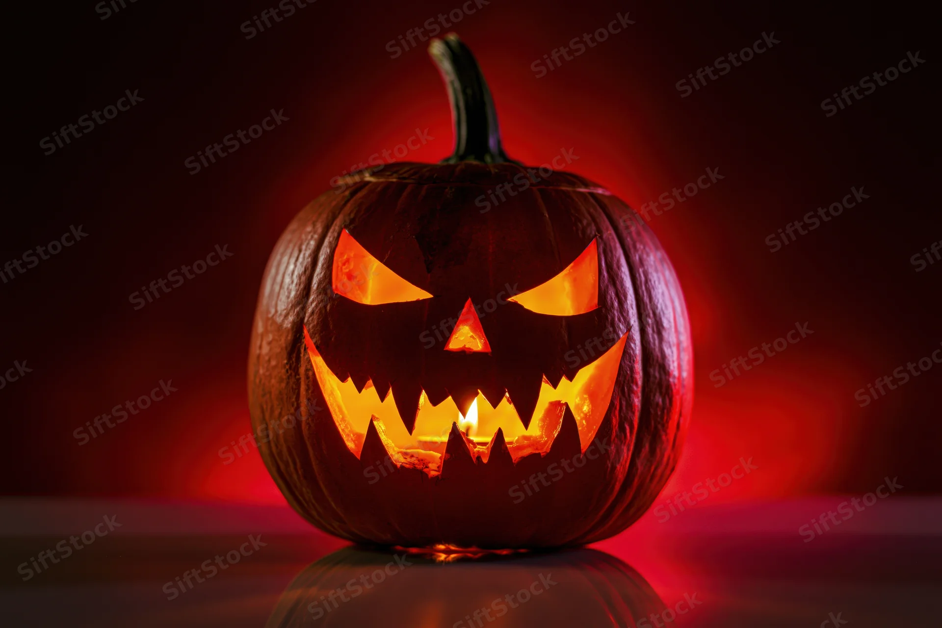 Carved pumpkin with glowing face lit from within on dark reflective surface