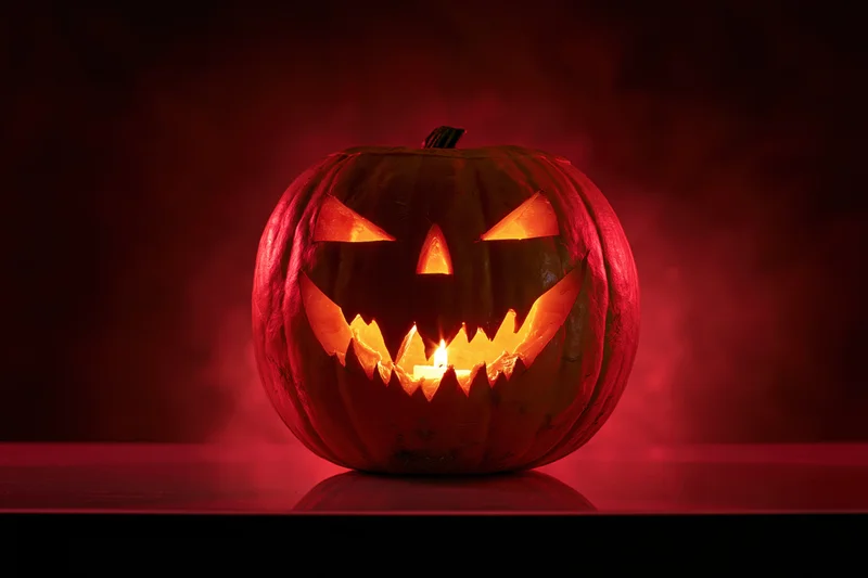 Carved pumpkin with glowing face lit by candle on dark surface in red smoke