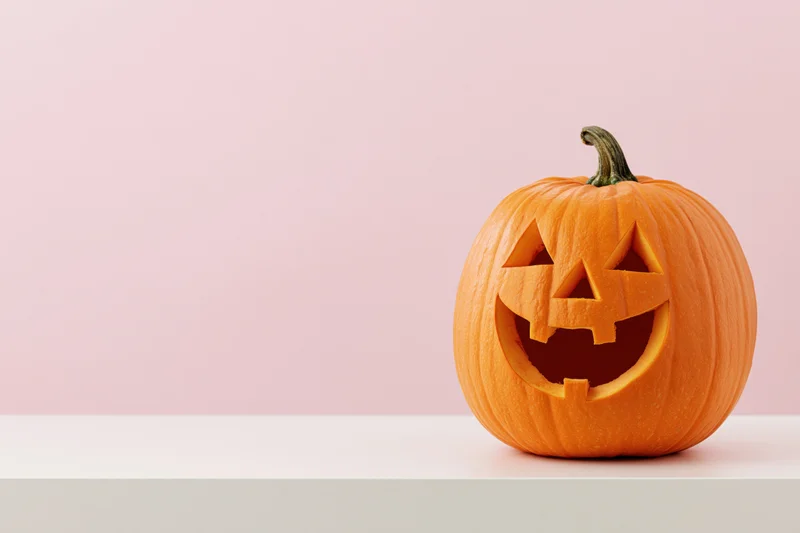 Carved jack-o-lantern with grinning face on white surface against pink background