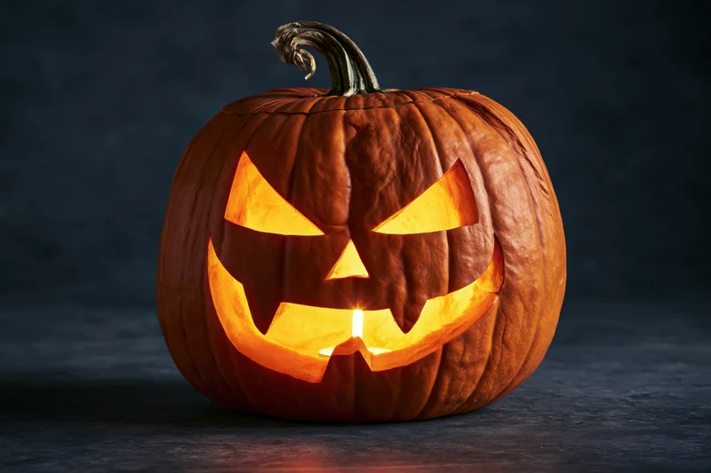 Carved pumpkin with jagged grinning face glowing from within on dark surface
