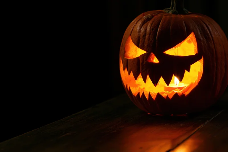 Carved pumpkin with jagged grin lit by candle on wooden table at night