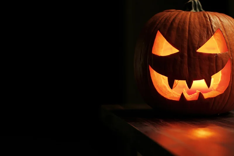 Carved pumpkin with glowing jagged grin on wooden table in dark setting