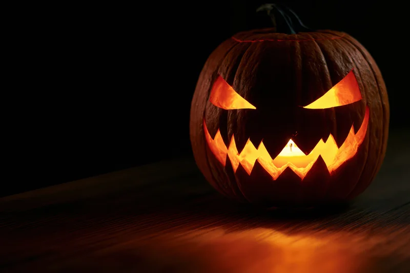 Carved pumpkin with jagged grin illuminated by candlelight on dark wooden surface
