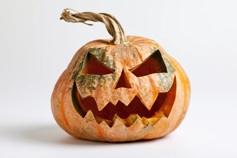 Carved pumpkin with jagged menacing face on white background