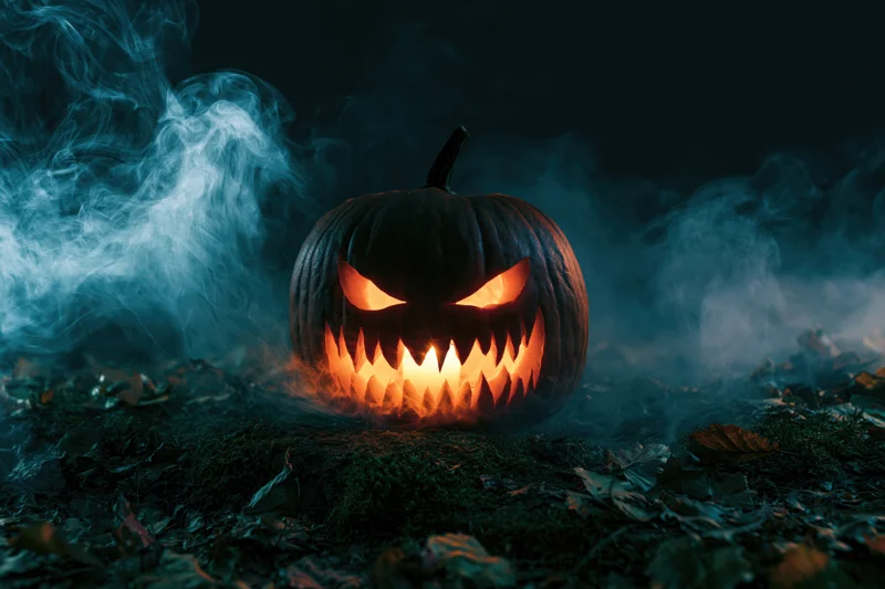 Carved pumpkin with jagged grin glowing in dark foggy forest at night