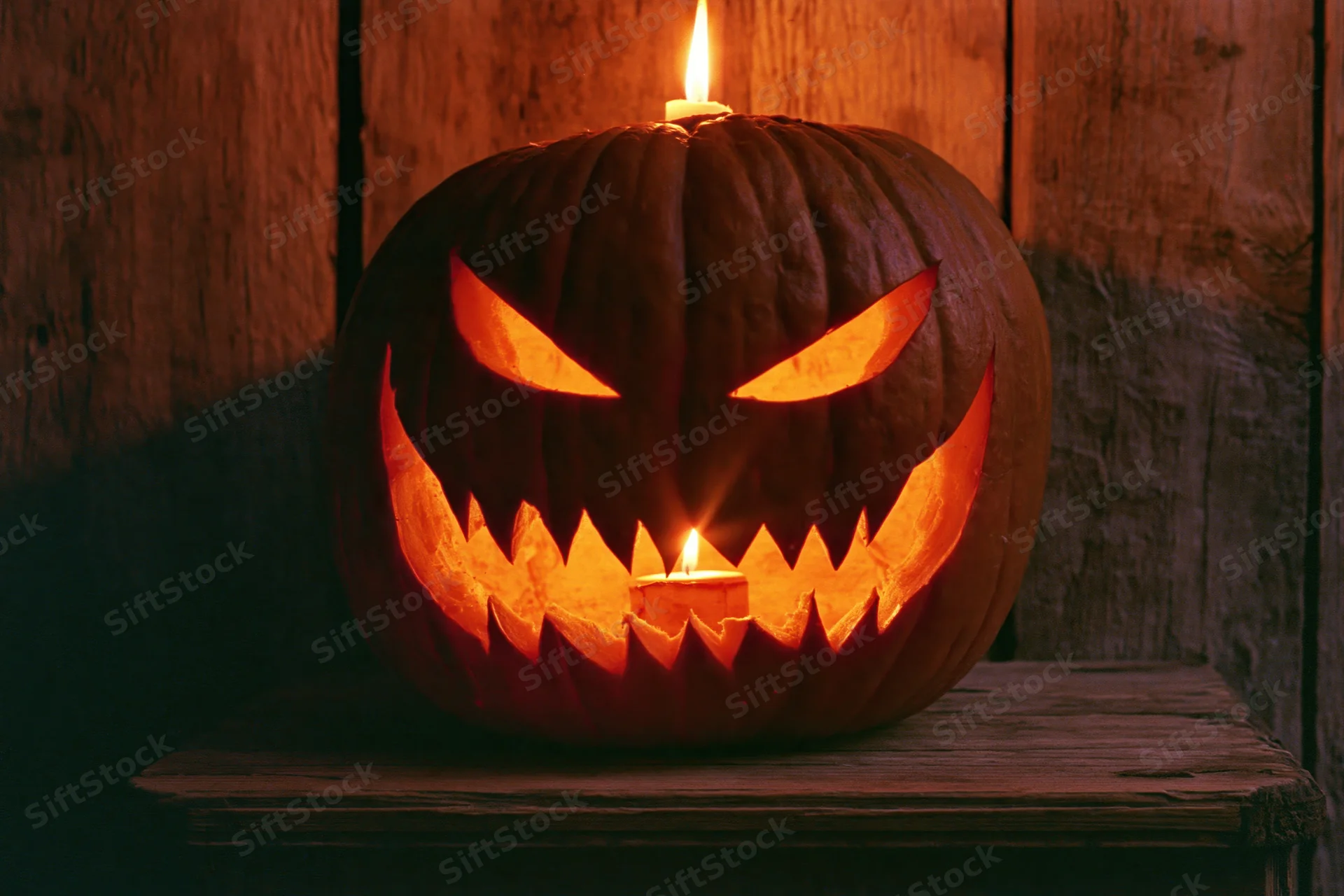 Carved pumpkin with menacing grin glowing from candles on wooden table
