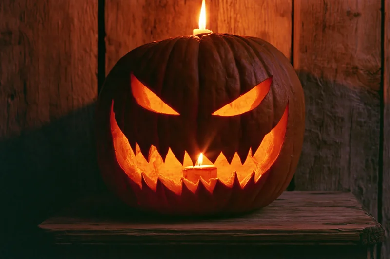 Carved pumpkin with menacing grin glowing from candles on wooden table