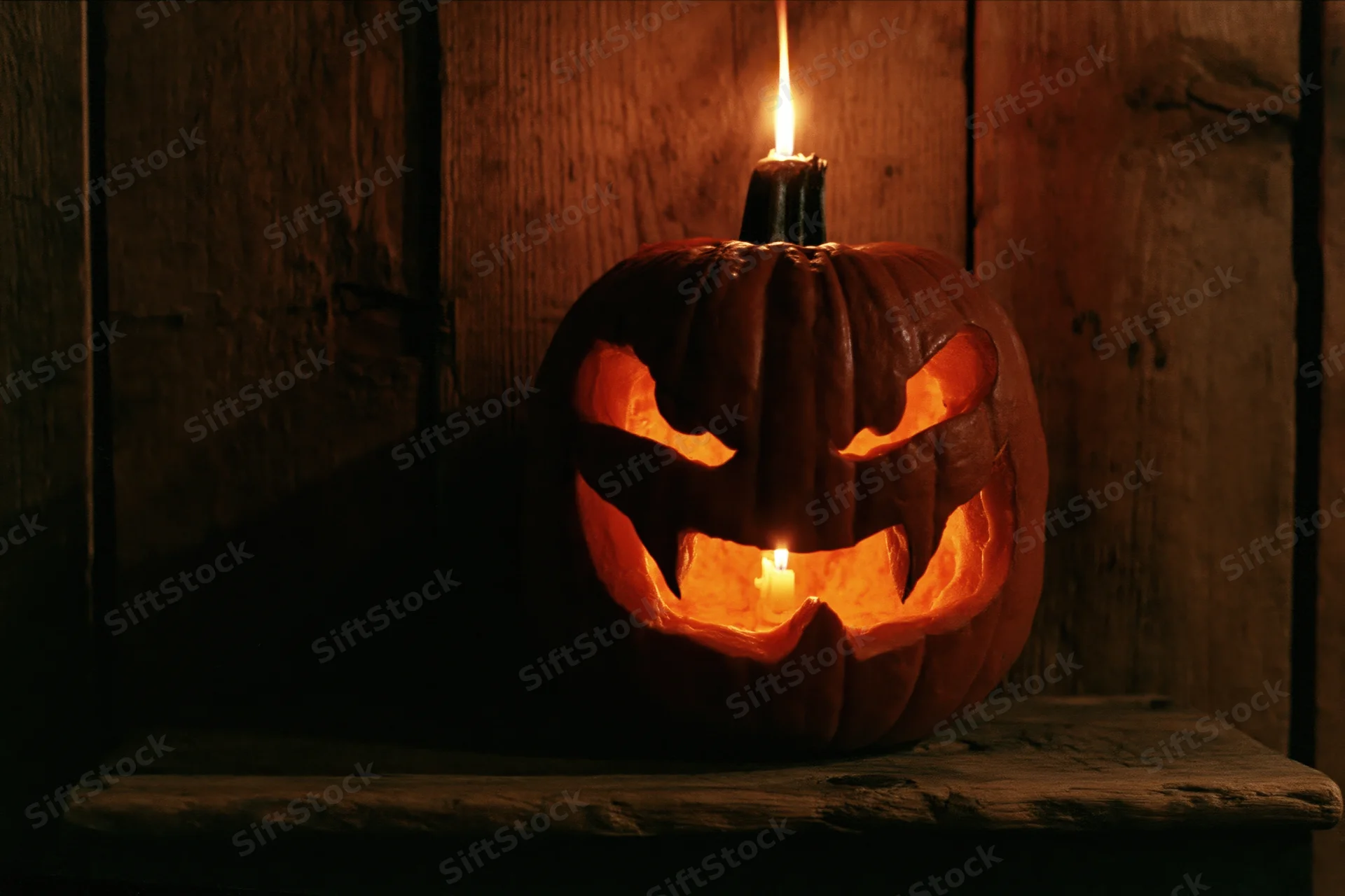 Carved pumpkin with glowing candle inside, placed on wooden surface against dark wood background