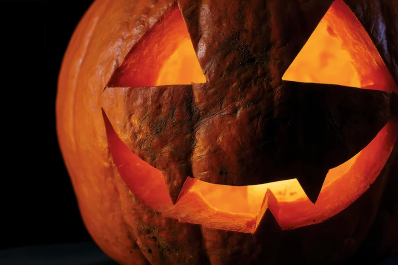 Carved pumpkin with triangular eyes and jagged smile glowing in the dark