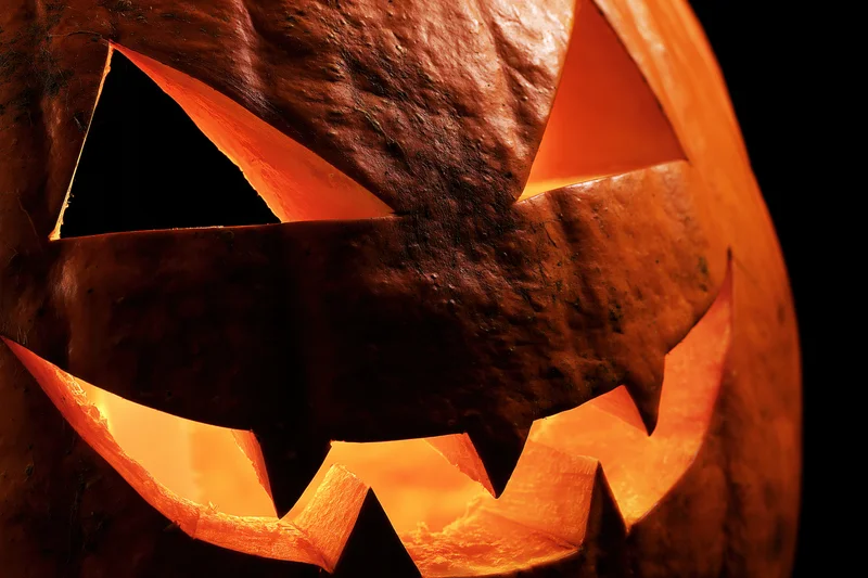Carved pumpkin with triangular eyes and jagged mouth glowing in the dark