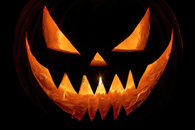Close-up of a carved pumpkin with glowing eyes and jagged grin lit from within at night