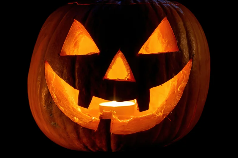 Carved pumpkin with triangular eyes and wide smile glowing from within at night