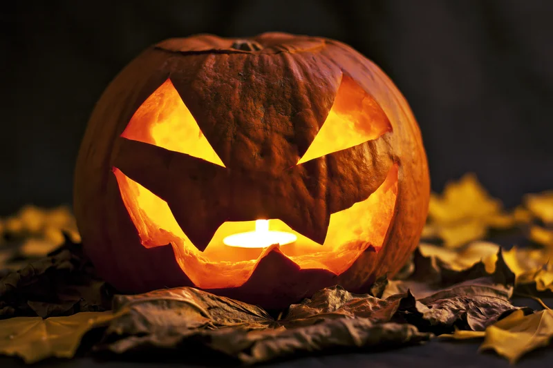 Carved pumpkin glowing from within on a bed of dry autumn leaves