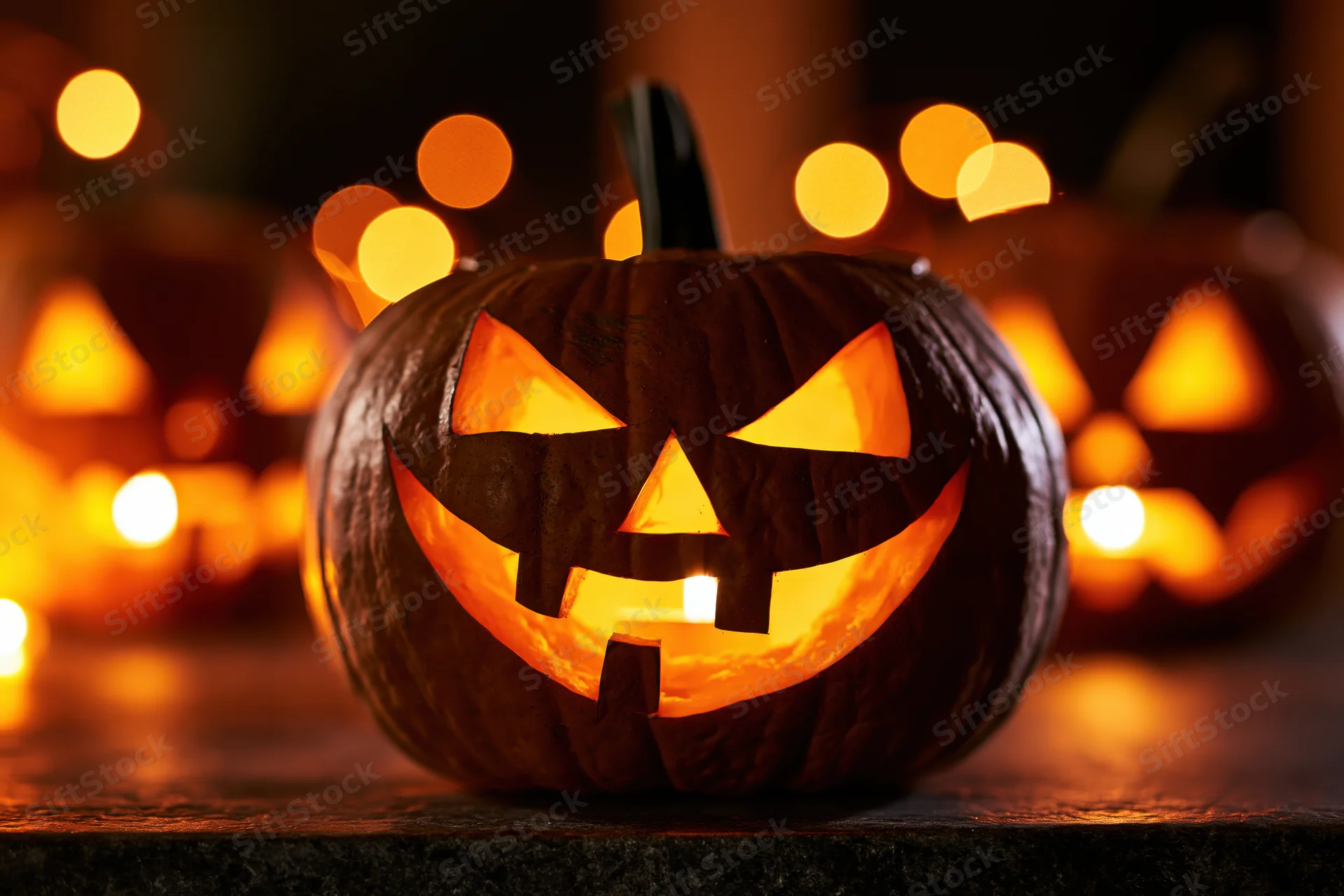 Carved jack-o-lantern glowing with orange candlelight on a stone surface at night