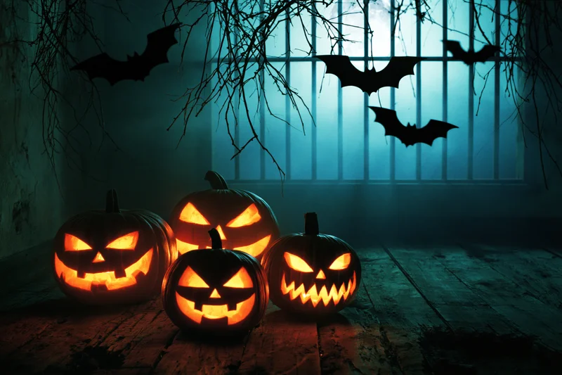 Carved jack-o-lanterns glowing on a rotting wooden floor near a barred window with bats and branches in a dark room