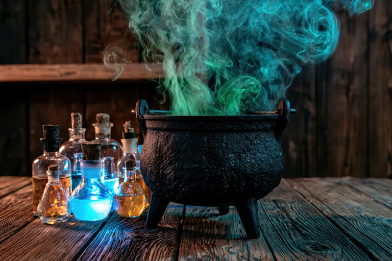 Cast iron cauldron emitting green and blue smoke on a wooden table surrounded by glass bottles of glowing potions
